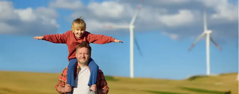 Et barn og en voksen foran to vindmøller